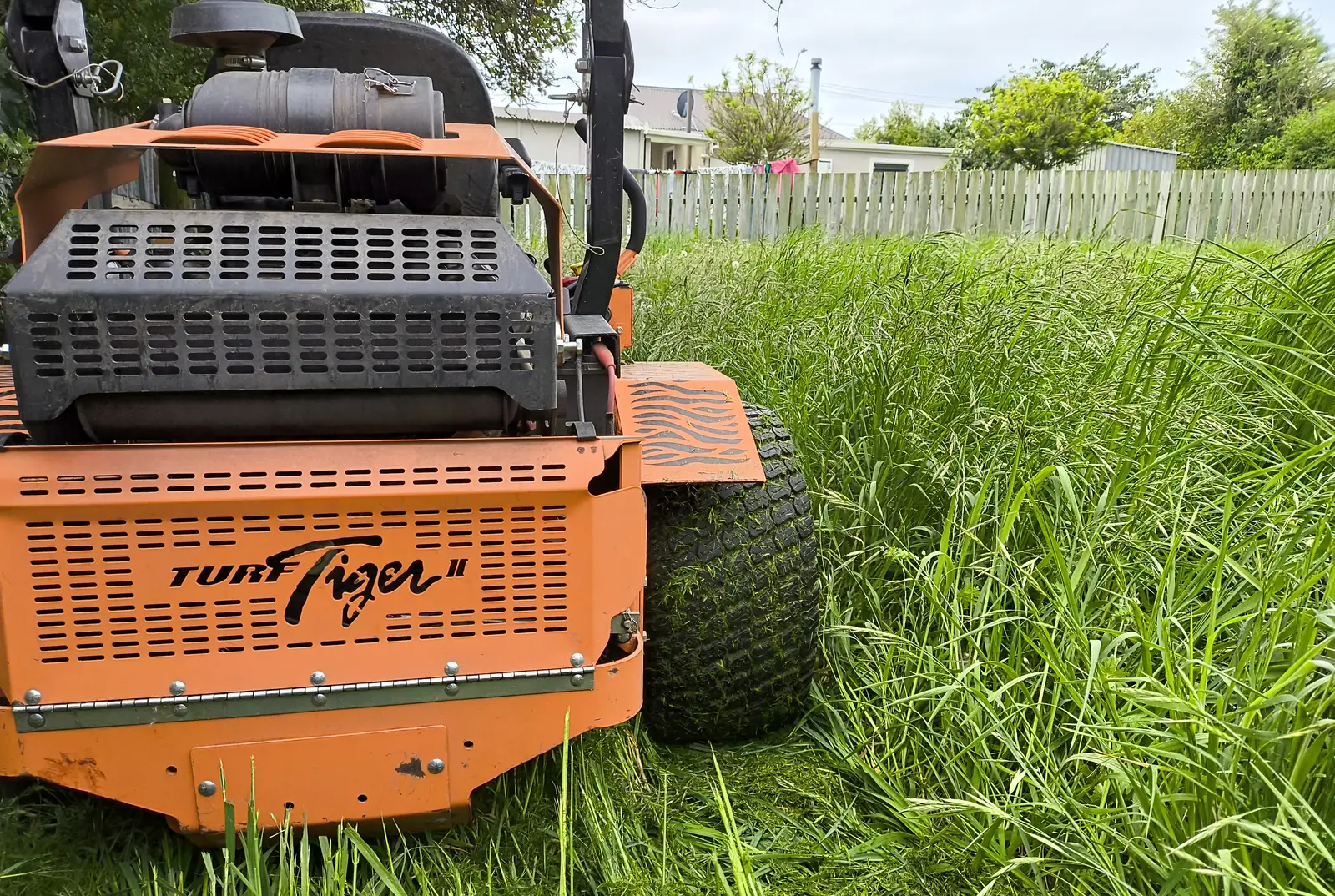 Side view of an orange Turf Tiger mower in long grass, with the freshly cut strip beside it